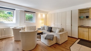 A modern living room with a sofa, armchairs, a coffee table, and a kitchen area with cabinets and a radiator. - Centrally Located and Quiet Trade Fair Apartment Berlin (Berlin)