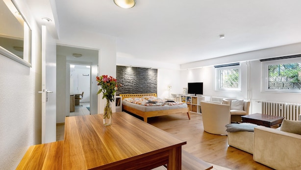 A modern living room with a wooden dining table, a sofa, a bed, and a stone accent wall. - Centrally Located and Quiet Trade Fair Apartment Berlin (Berlin)