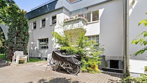 A building with a white exterior, a covered bicycle, a bench, and a small garden area. - Centrally Located and Quiet Trade Fair Apartment Berlin (Berlin)