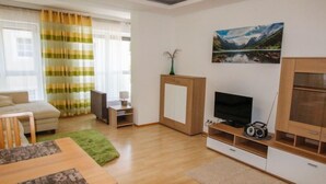Een moderne woonkamer met een bank, televisie, houten kast en een schilderij van een berglandschap.