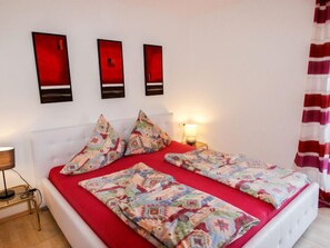 A bed with red bedding, a white headboard, and patterned pillows. There are three wall-mounted red panels above the bed.