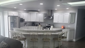 Una cucina moderna con mobili bianchi, elettrodomestici in acciaio inossidabile e un'isola centrale con sgabelli da bar.