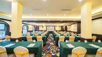 A conference room with rows of tables, each with a green tablecloth and white chairs tied with yellow sashes.