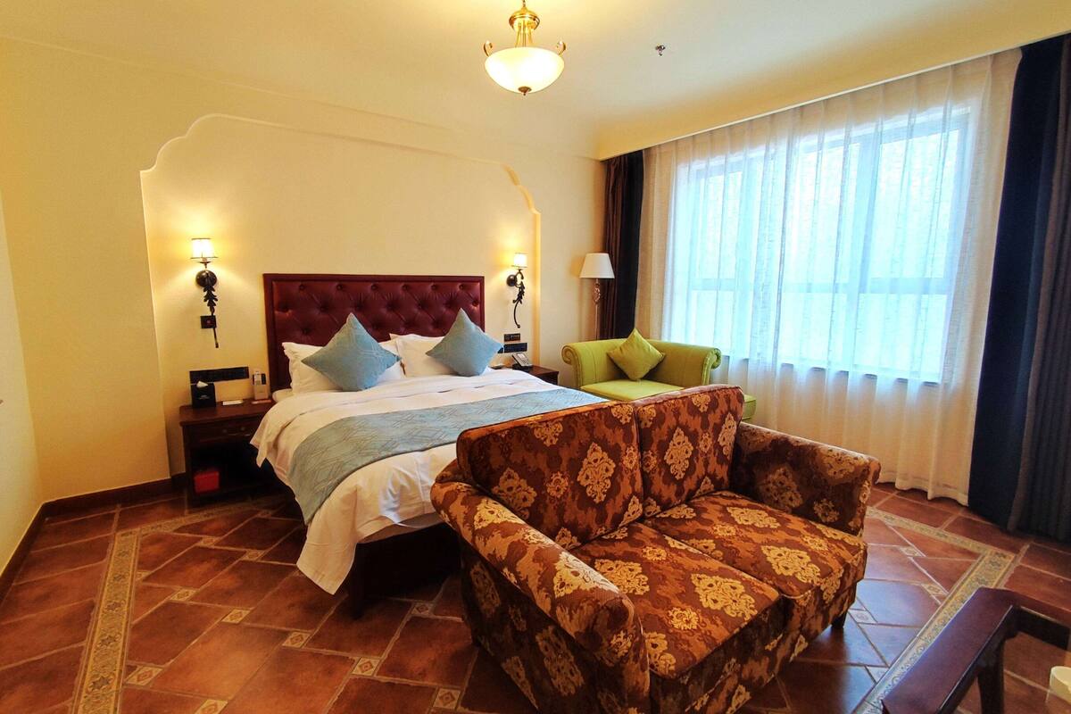 Une chambre d’hôtel avec un grand lit, un canapé, une table de chevet et une fenêtre avec des rideaux.