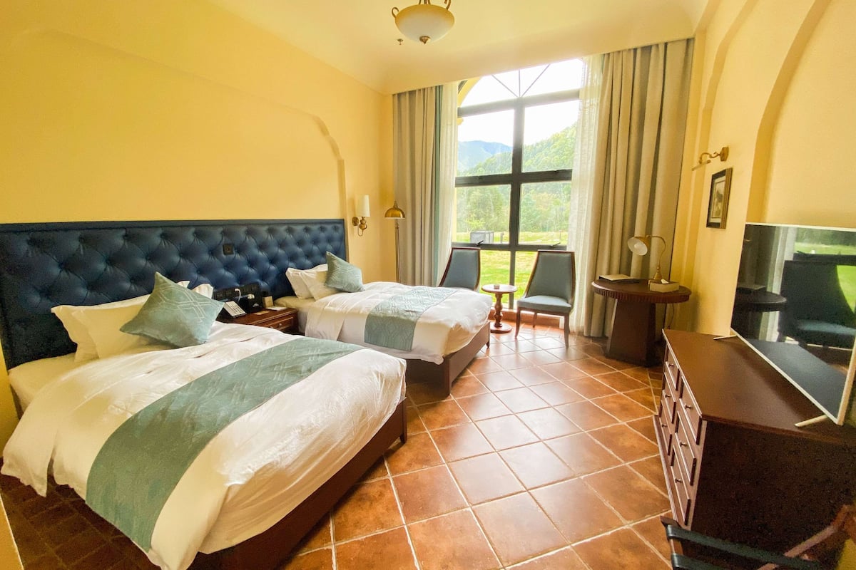 Une chambre d’hôtel avec deux lits, une télévision, un bureau et une vue sur l’extérieur.