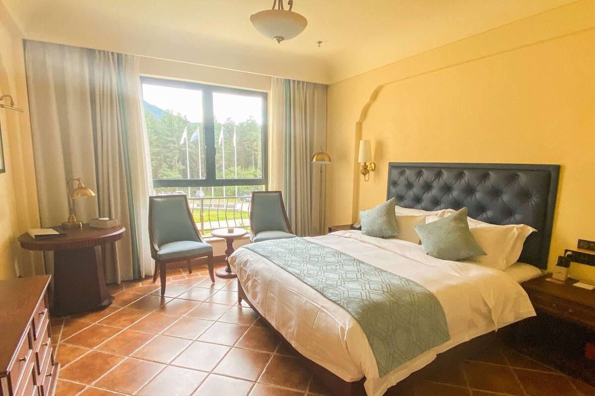 Une chambre d’hôtel avec un grand lit, un bureau, une chaise et une vue sur l’extérieur par une fenêtre.