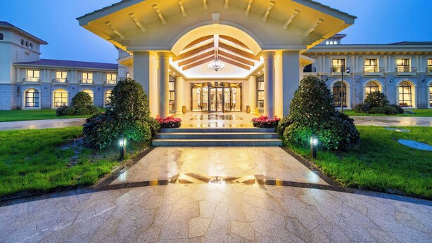 A grand entrance with a covered walkway, a central chandelier, and a symmetrical facade with multiple windows and balconies. - Howard Johnson by Wyndham Yaan Forest Resort (Ya'an)