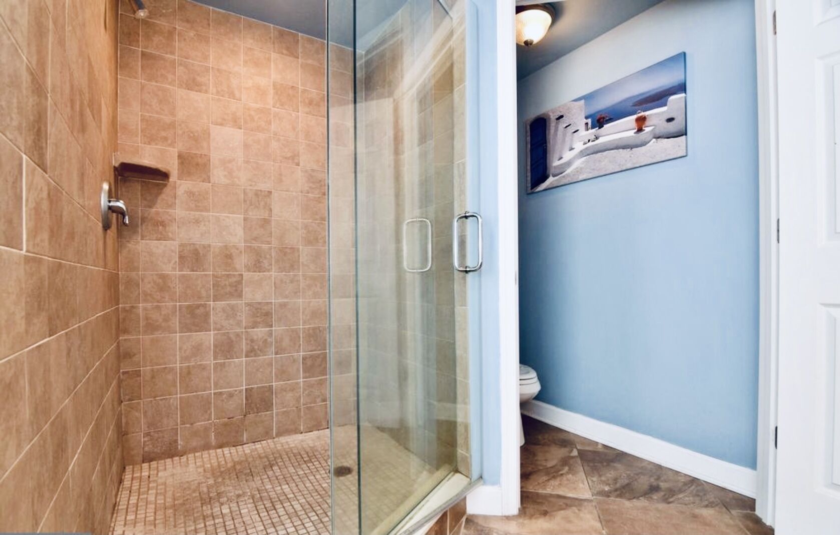 A bathroom with a glass shower enclosure, tiled walls, and a blue accent wall with a painting.