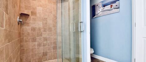 A bathroom with a glass shower enclosure, tiled walls, and a blue accent wall with a painting.