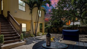 Un patio con una mesa dispuesta para dos personas, una botella de vino y una silla azul.