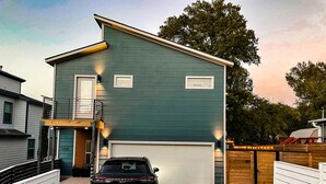 Een huis met twee verdiepingen, een garage, een zwarte SUV ervoor geparkeerd, en een houten omheining rond het terrein.