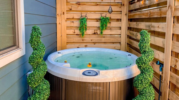 Een hottub met een houten terras, omringd door een houten omheining en begroeiing.