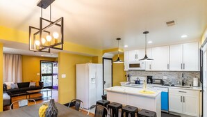 Uma cozinha moderna com armários brancos, uma ilha central e uma área de refeições com mesa e banquetas.