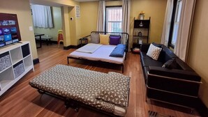 Quarto de hotel compacto com cama, sofá, mesinha e televisão.
