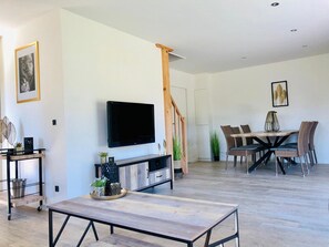 Un soggiorno moderno con una televisione a schermo piatto, un tavolo da pranzo con sedie, una scala e un arredamento minimalista.