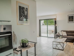 Una cocina moderna con horno integrado, un comedor con mesa de vidrio y una sala de estar con sofá y mesa de centro.