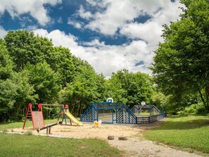 A playground with a slide, climbing structures, and a basketball hoop in a park.