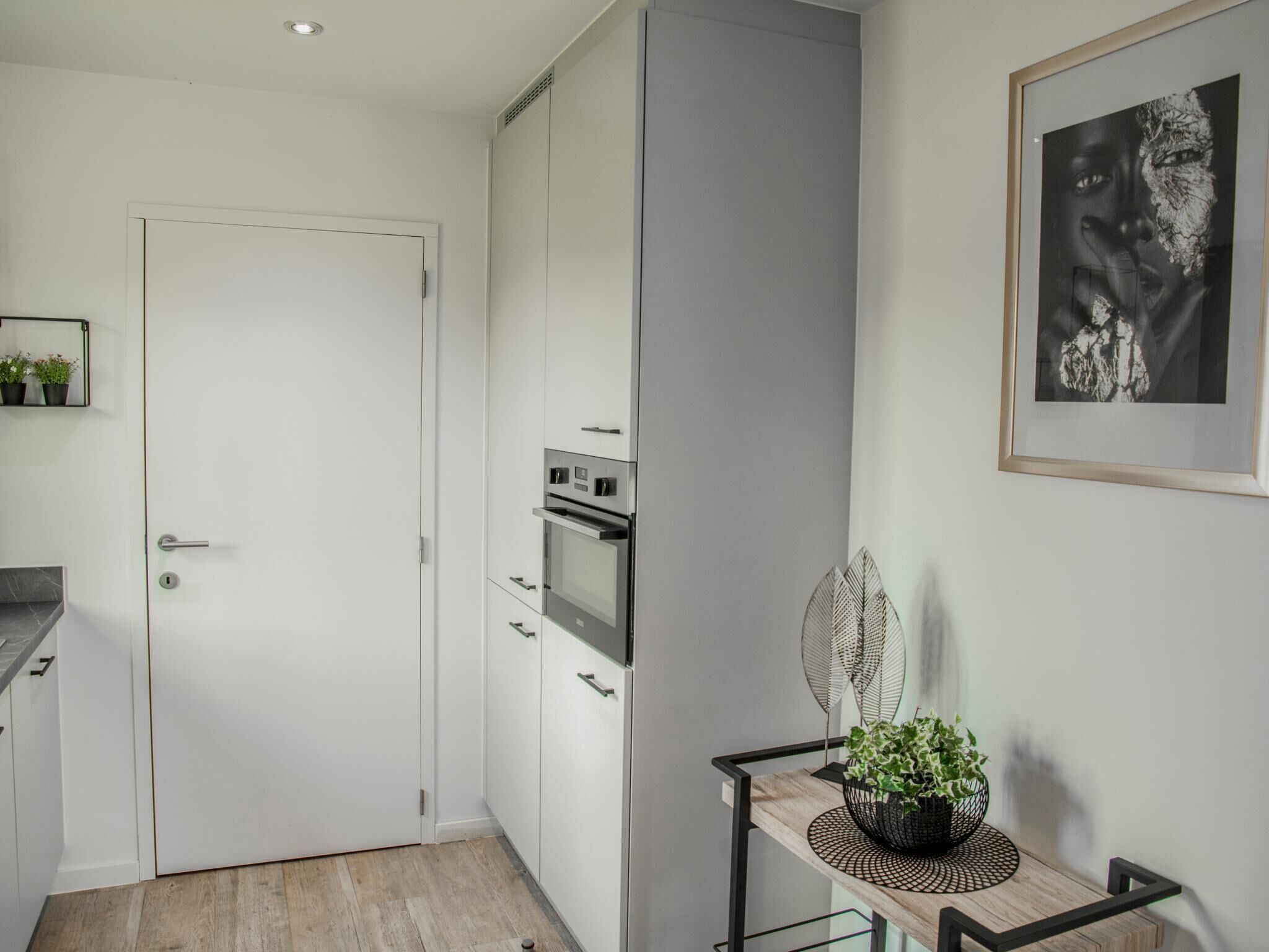 A modern kitchen with white cabinets, a built-in oven, and a small dining table with a plant.