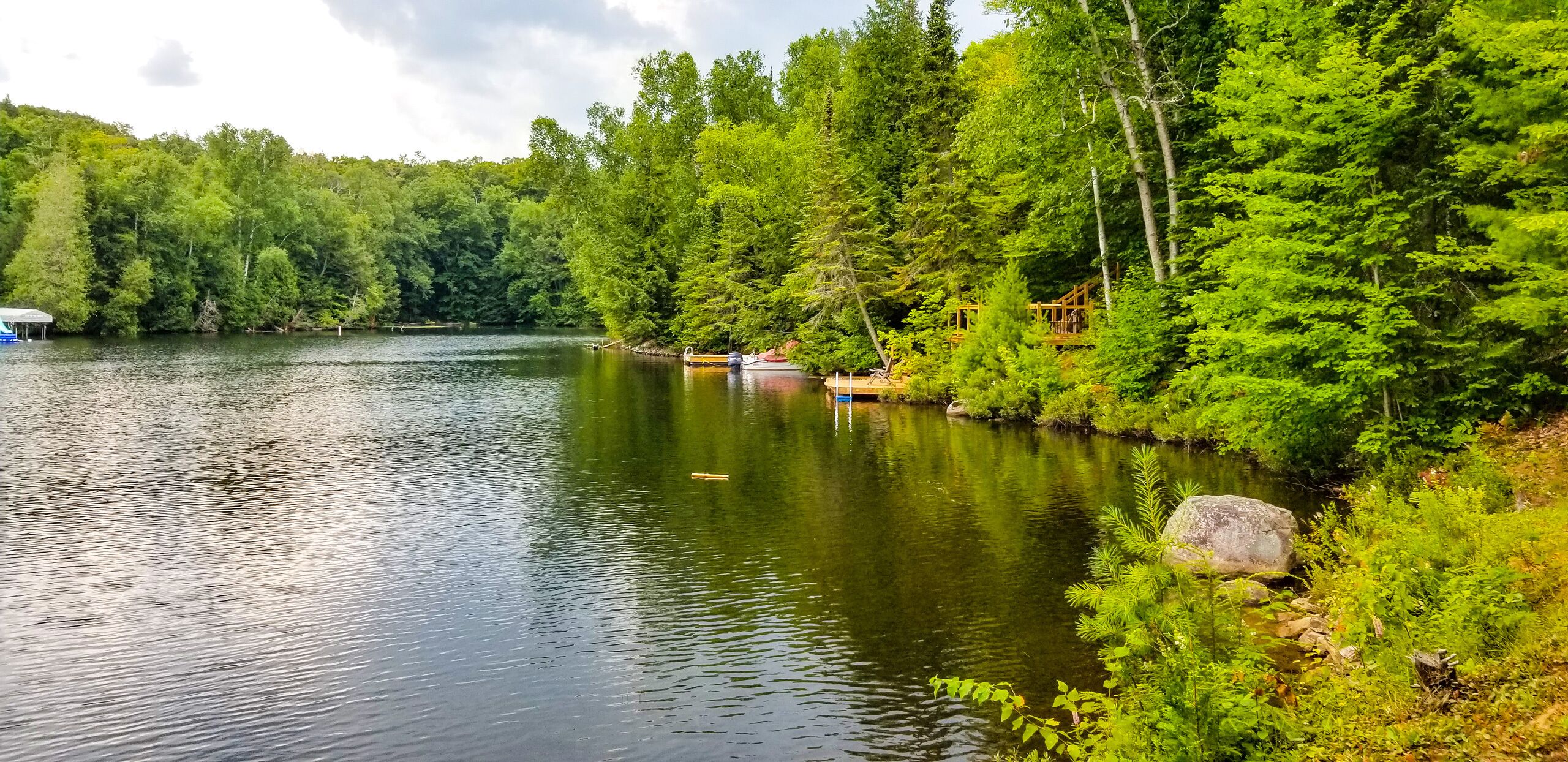 Um lago tranquilo rodeado por floresta densa, com um cais e um pequeno barco.