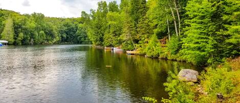 Um lago tranquilo rodeado por floresta densa, com um cais e um pequeno barco.