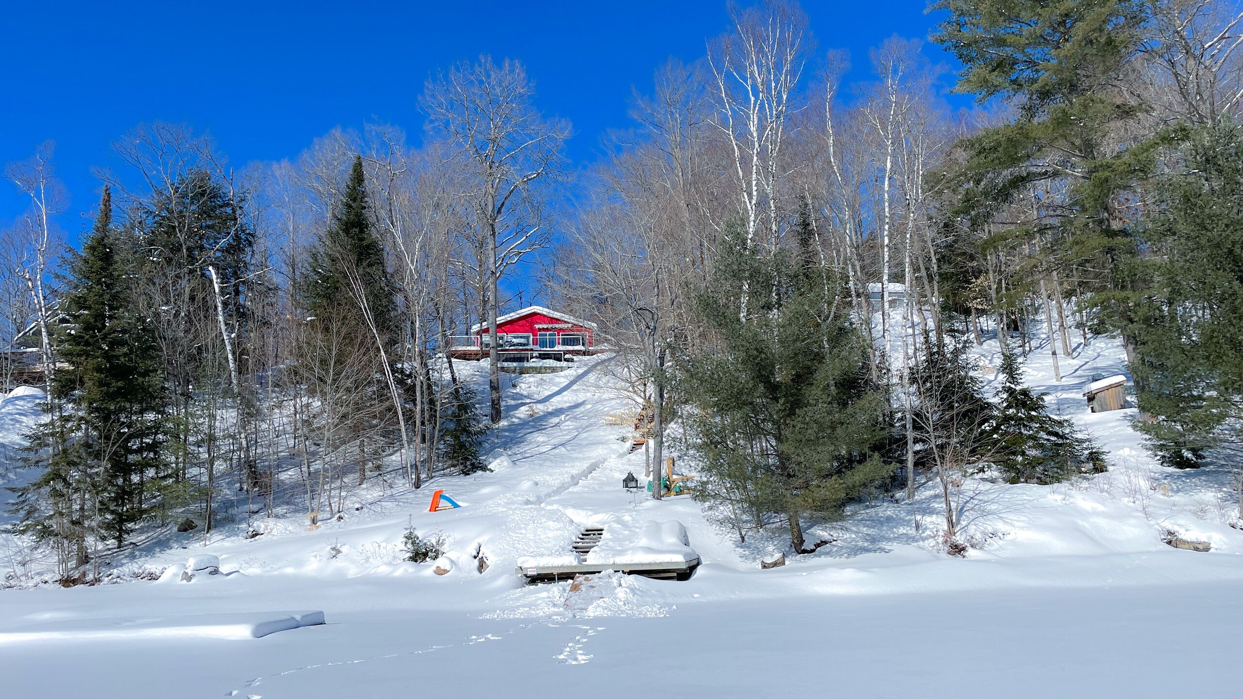 Un paysage enneigé avec un bâtiment rouge au sommet d’une colline, entouré d’arbres.