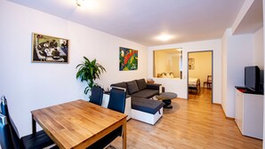 A modern living room with a wooden dining table, a sofa, a potted plant, and artwork on the walls.