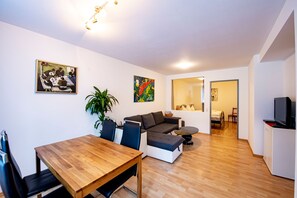A modern living room with a wooden dining table, a sofa, a potted plant, and artwork on the walls.