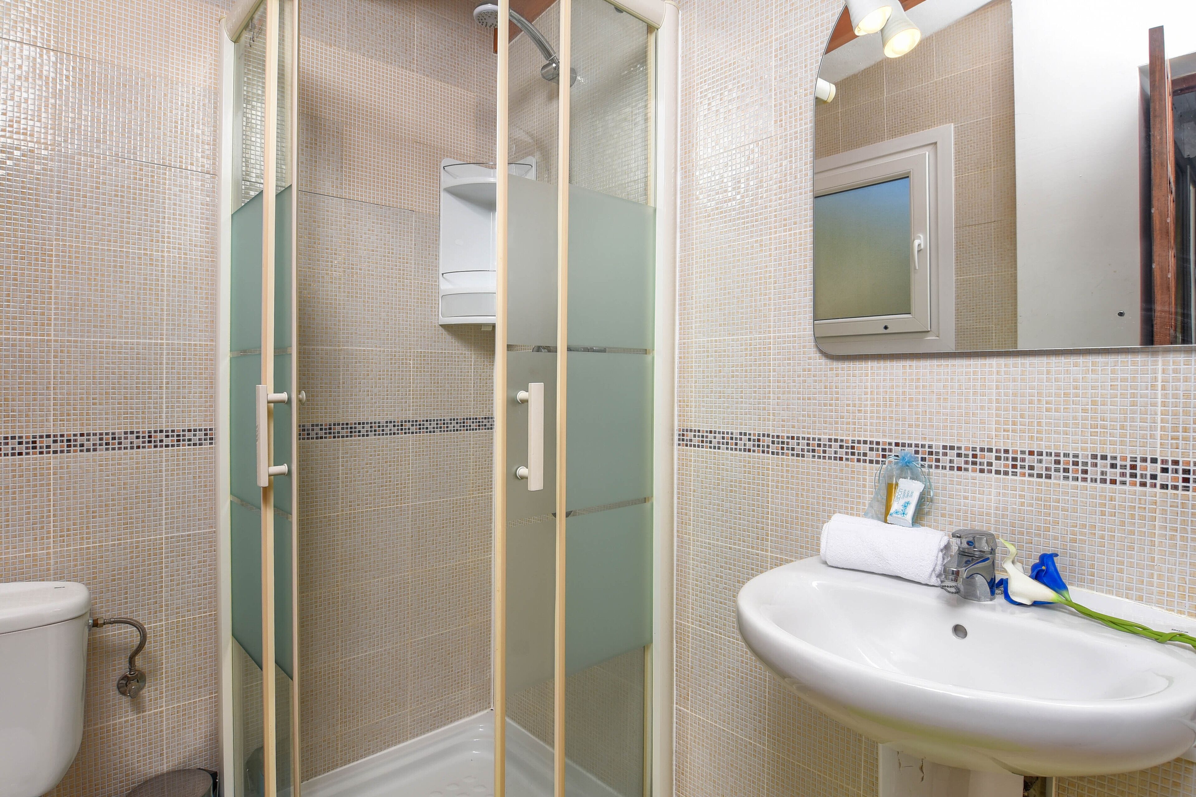 A bathroom with a glass-enclosed shower, a sink with a mirror, and tiled walls.