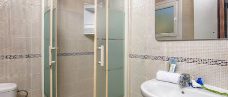 A bathroom with a glass-enclosed shower, a sink with a mirror, and tiled walls.