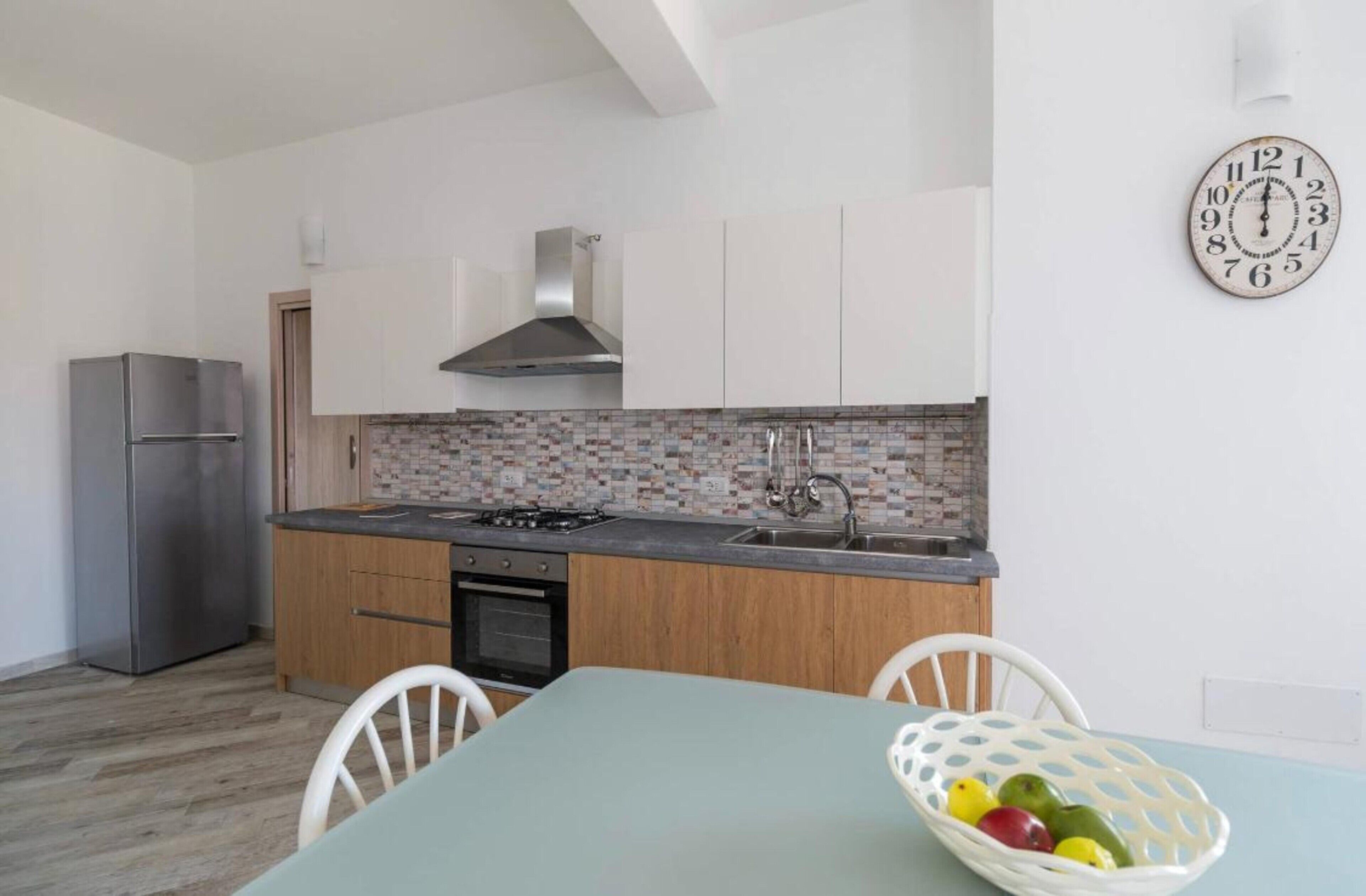 Une cuisine moderne avec des armoires blanches, une hotte de cuisinière en acier inoxydable, un pare-feu en carrelage et une horloge murale.