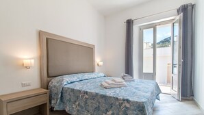 A bedroom with a bed, bedside table, wall-mounted lights, and a view through a sliding glass door. - Apartment Blu with Mountain View, Balcony, A/C & Wi-Fi (DORGALI)