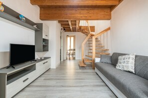 A modern living room with a flat-screen TV, grey sofa, wooden staircase, and a hallway leading to another room. - Holiday Home 'Mary' with Balcony and Air Conditioning (Carloforte)