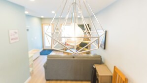 A modern interior with a geometric hanging light fixture, a sofa, and a wooden table.