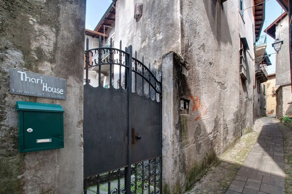 Une ruelle étroite, fermée par un portail, avec une enseigne indiquant « Thari House » et un coffret électrique vert.
