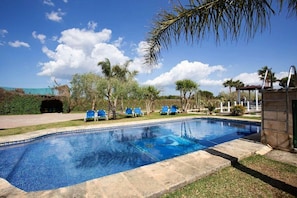 Ein Swimmingpool mit blauen Fliesen, umgeben von Liegestühlen und Palmen.