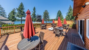 Una terraza de madera con mobiliario exterior, incluidas mesas y sillas, y sombrillas rojas.