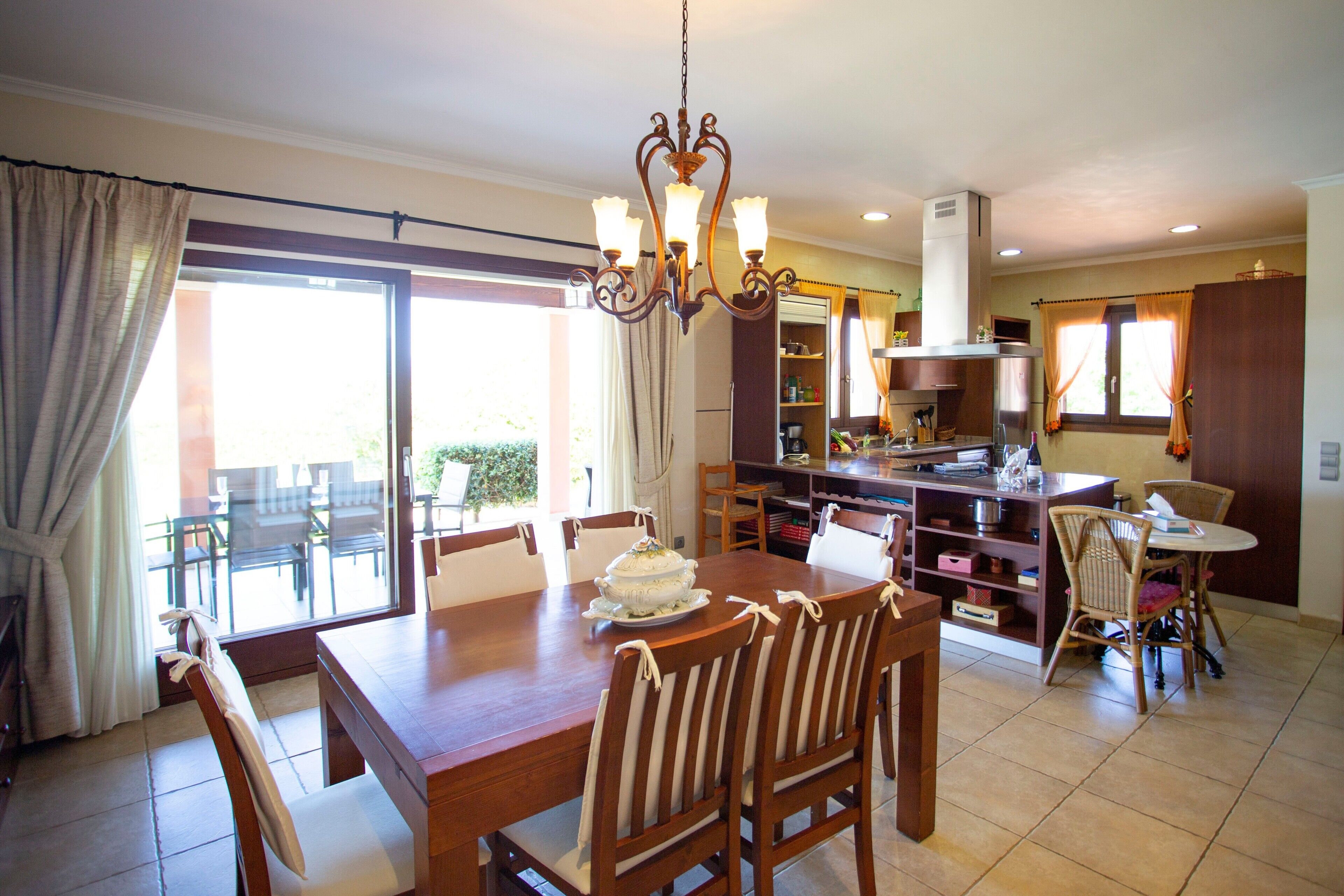 A dining area with a wooden table and chairs, a chandelier, and a view through a glass door to the outside.