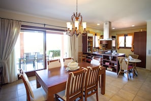 Un comedor con mesa y sillas de madera, una araña y vistas al exterior a través de un ventanal.