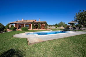 Una casa con piscina, patio y sombrilla de paja.