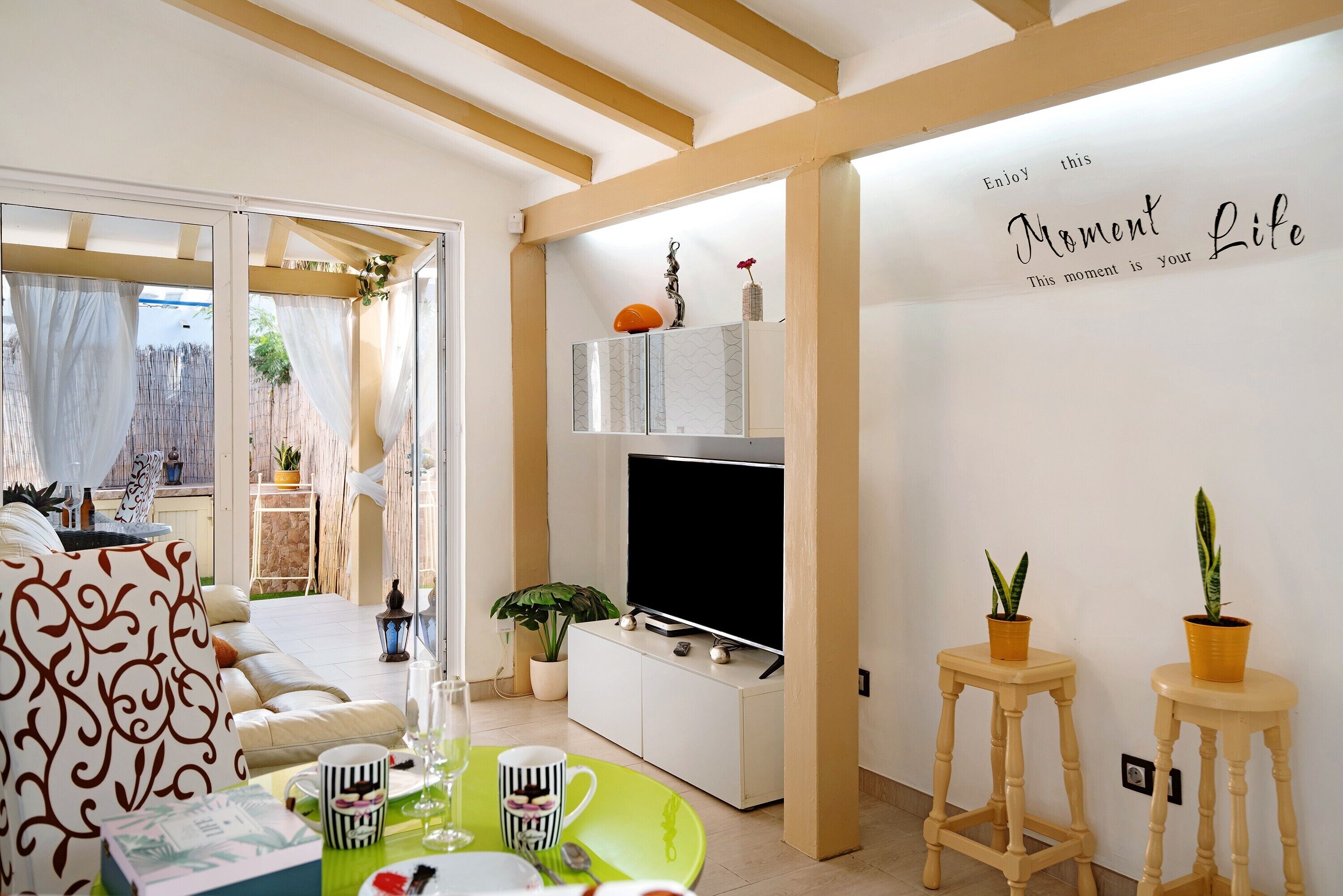 Una sala de estar con un sofá, una mesa de comedor con sillas, un televisor y dos plantas en macetas.