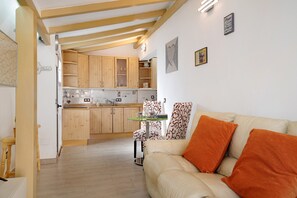 Un espacio habitable compacto con kitchenette, una zona de comedor con mesa y sillas, y un sofá con cojines naranjas.