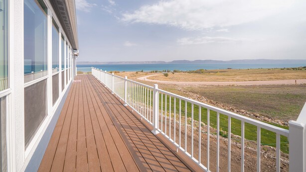 A wooden deck with white railings overlooking a coastal landscape.