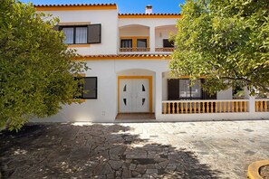Un edificio de dos pisos con un patio empedrado de piedra, paredes blancas y detalles en naranja.