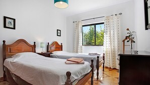A bedroom with two wooden beds, a window with curtains, a desk, and a dresser.