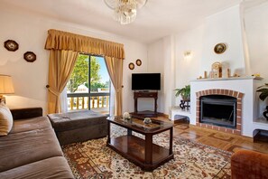 A living room with a sofa, a coffee table, a fireplace, a TV, and a patterned rug. - Vacation Home Vivenda Ribeiro - A with Mountain View, Fireplace, Wi-Fi, Garden, Terrace & Balcony (Lagos)