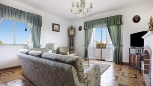 A living room with a sofa, a chandelier, a clock, and a television.