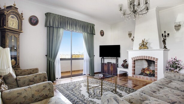 A living room with a sofa set, a television, a fireplace, and a large window with curtains.