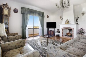 Ein Wohnzimmer mit einer Sofagarnitur, einem Fernseher, einem Kamin und einem großen Fenster mit Vorhängen.