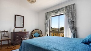 A bedroom with a bed, a dresser, a chair, a mirror, and a window with curtains.