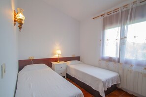 A room with two single beds, a nightstand with a lamp, a wall-mounted light fixture, and a window with sheer curtains. - Club Villamar - Holiday home for 5 with communal pool (Sant Antoni de Calonge)